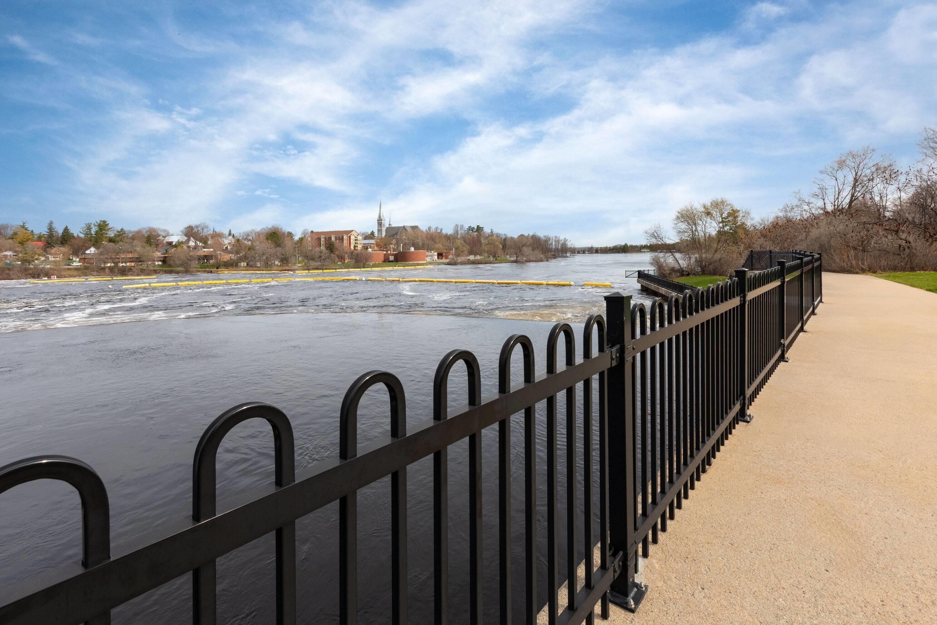 A river with a bridge, a walkway, and buildings in the background.
