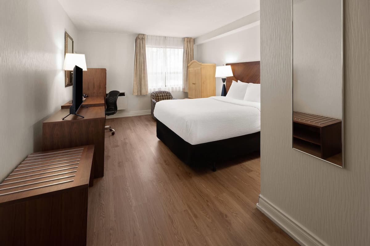 A hotel room with a bed, desk, chair, wardrobe, and a mirror.