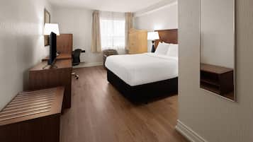 Una habitación de hotel con cama, escritorio, silla, armario y espejo.