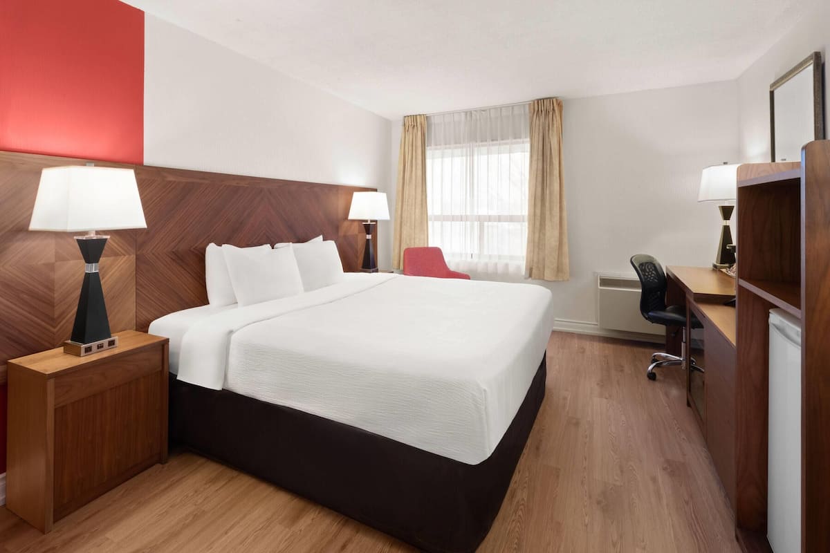 A hotel room with a bed, a desk, a chair, a lamp, and a window with curtains.
