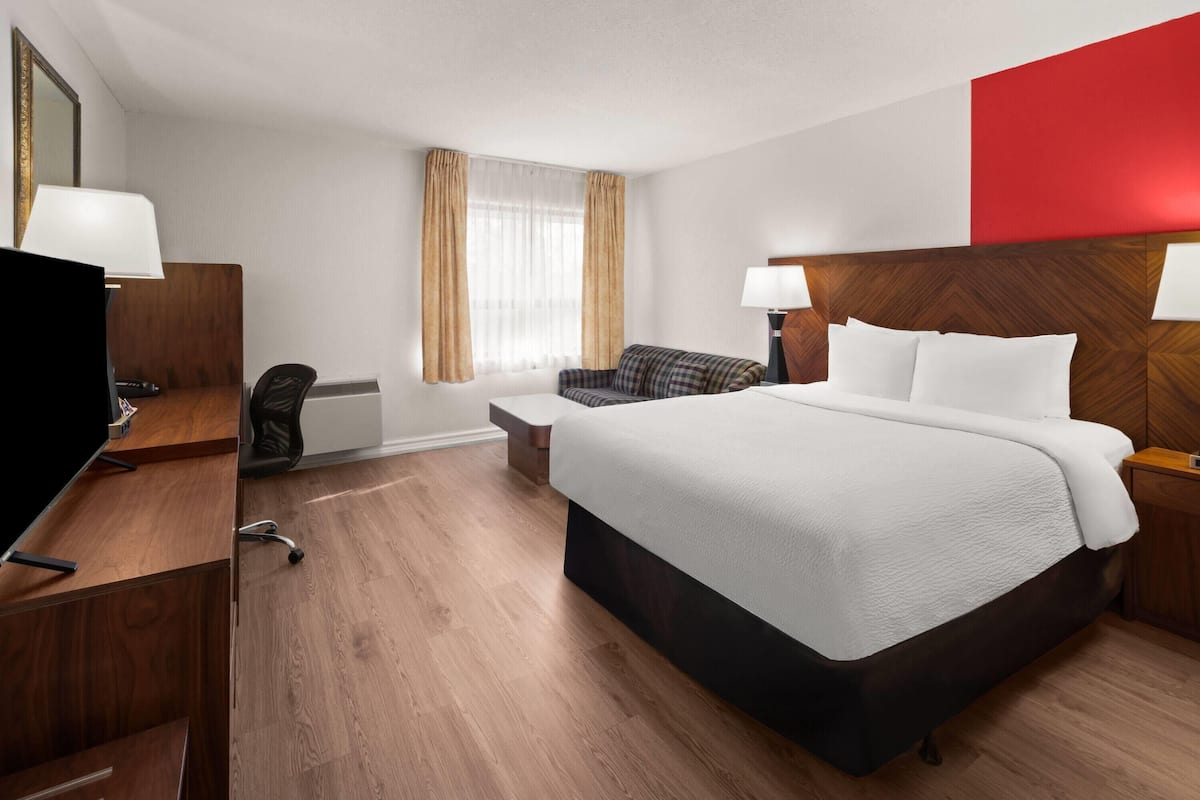A hotel room with a bed, a desk with a TV, a chair, a nightstand, and a window with curtains.