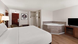 Habitación de hotel con una cama grande, baño con bañera, televisión y suelo de madera.