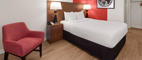 Una habitación de hotel con una cama, dos lámparas de noche, una silla roja, una mesita de noche de madera y un cuadro en la pared.