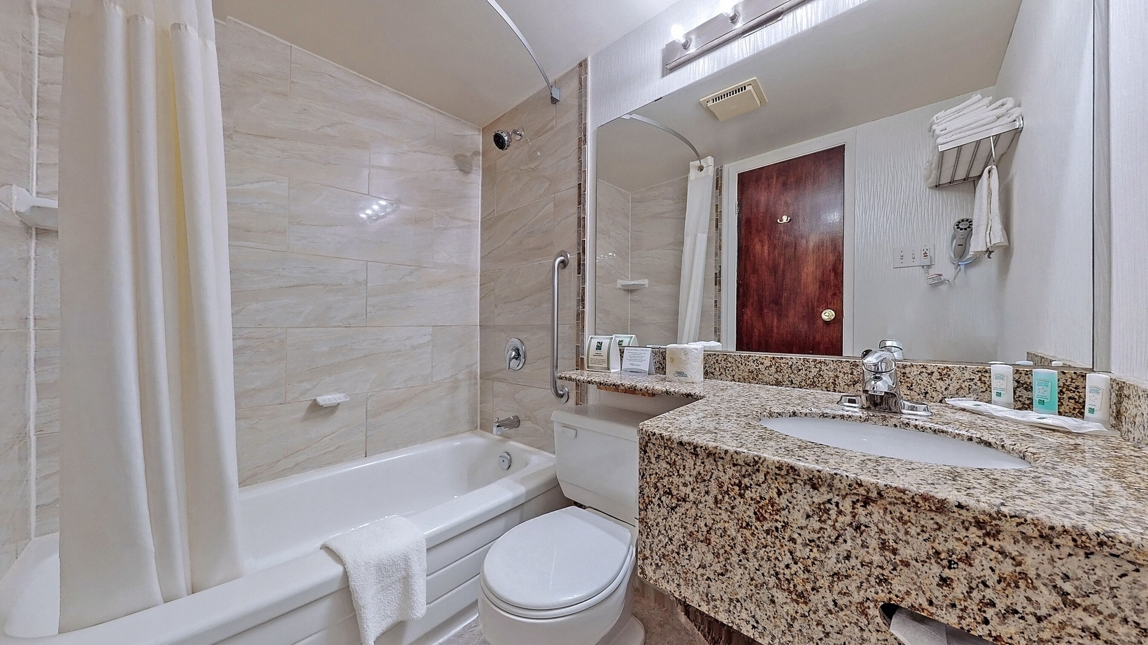 A modern bathroom with a bathtub, toilet, and granite countertop.