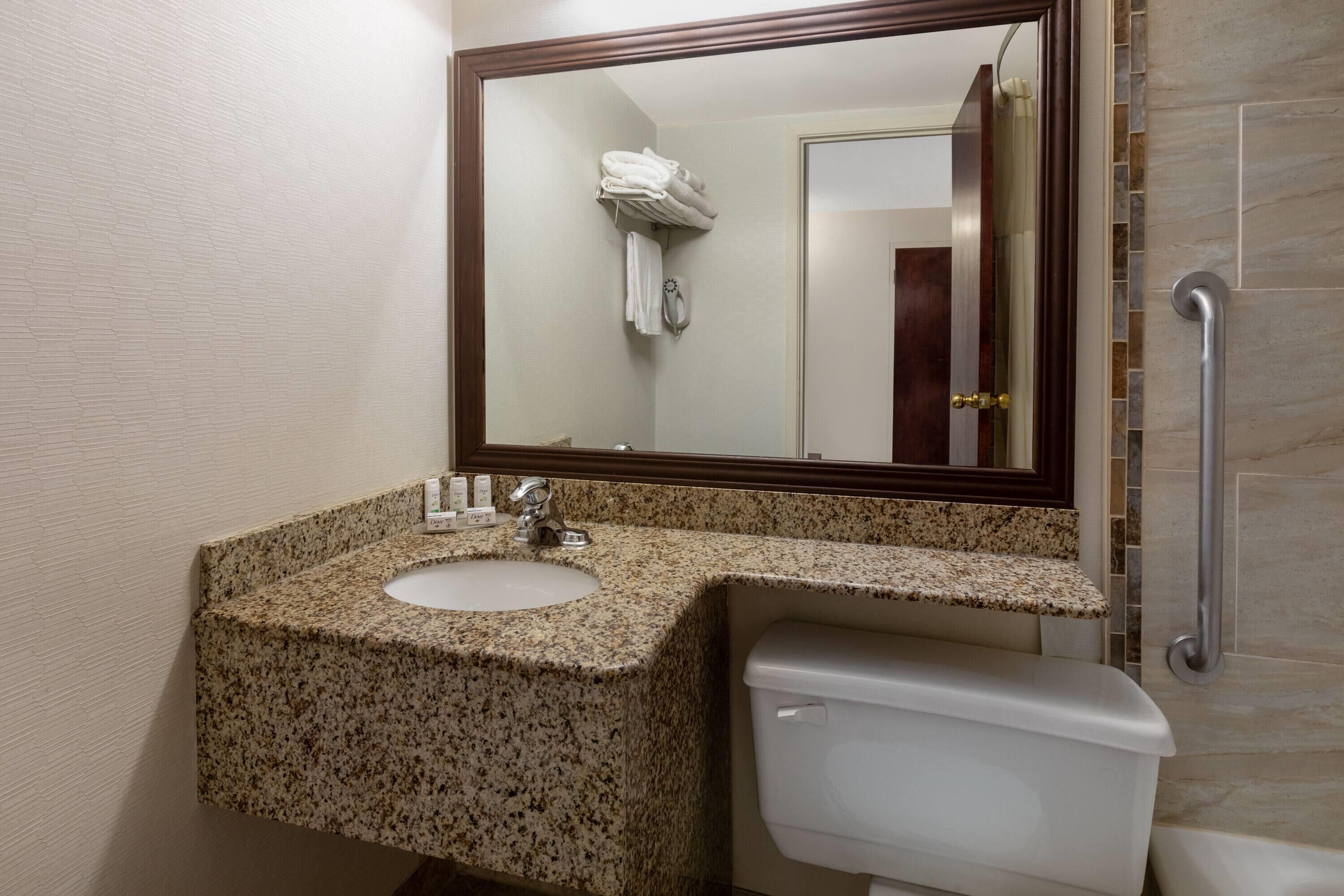 Un baño con lavamanos de encimera de granito, inodoro, espejo y zona de ducha.