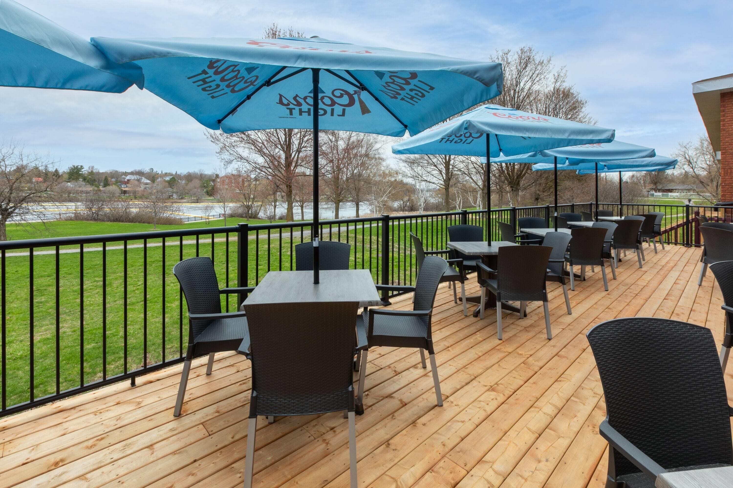 A deck with outdoor seating, umbrellas, and a view of a grassy area.