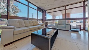 Un espacio interior amplio con un sofá color beige, una mesa de centro de vidrio y un sillón de tonos claros. Grandes ventanales ofrecen vistas al exterior.