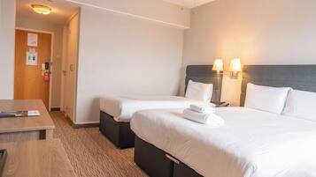 A hotel room with two beds, a desk, and a chair. There are two wall-mounted lamps and a ceiling light.