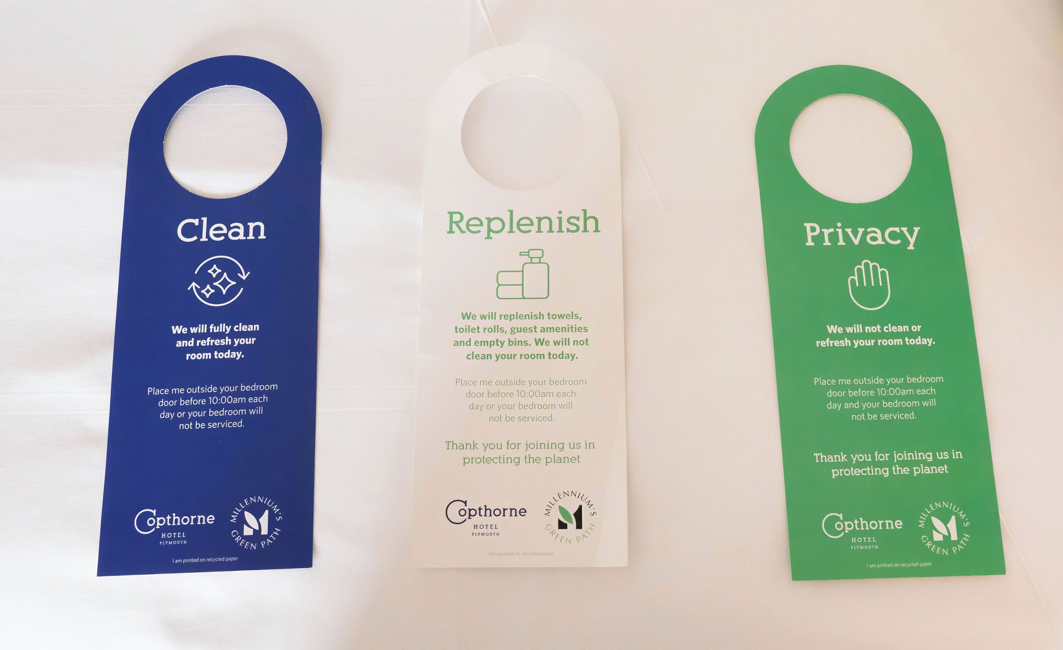 Three hotel room tags with different messages: 'Clean,' 'Replenish,' and 'Privacy.' Each tag has a hole for hanging and includes the hotel's logo and a recycling symbol.