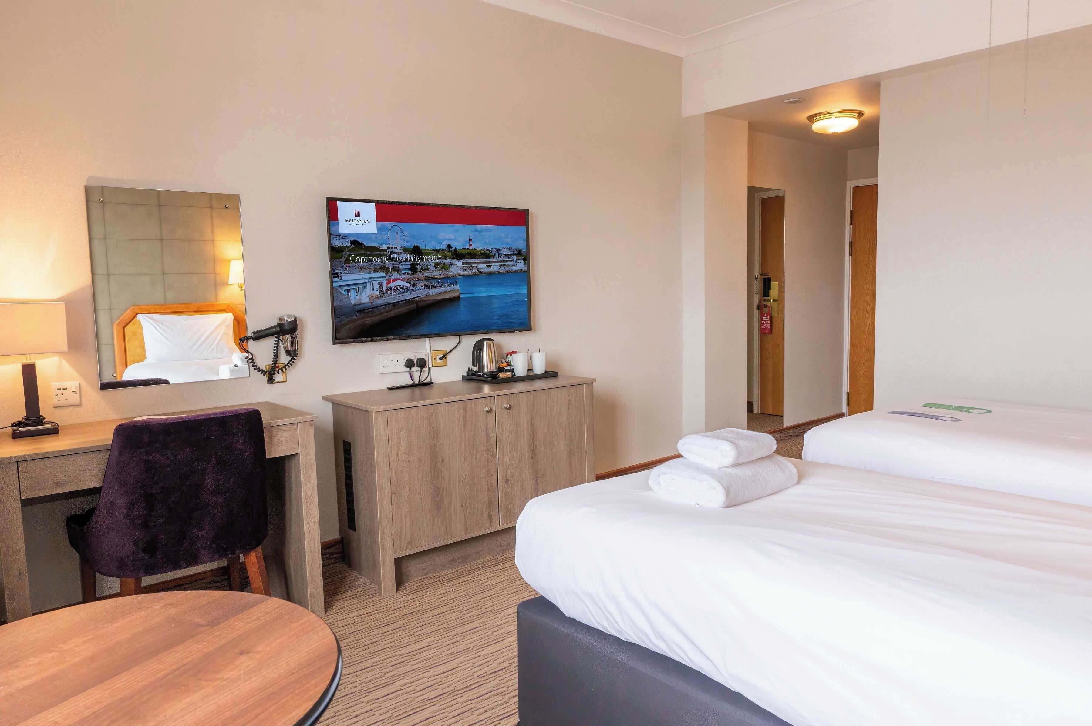 A hotel room with a bed, a desk with a chair, a television, and a small cabinet.