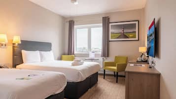 A hotel room with two beds, a desk, a chair, a TV, and a window with a view of a lighthouse.