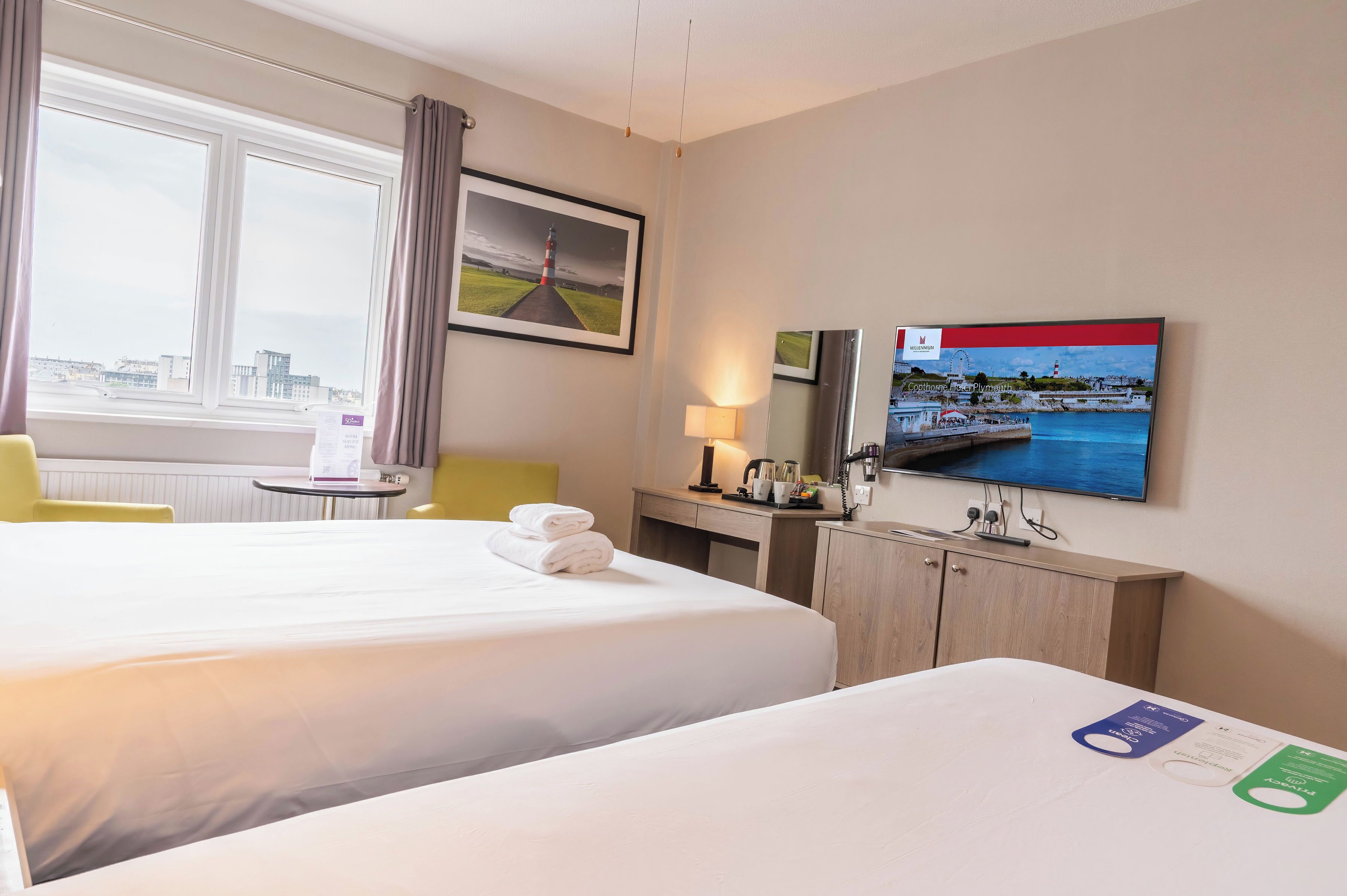 A hotel room with two beds, a desk, a chair, a TV, and a window with a city view.