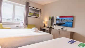 A hotel room with two beds, a desk, a chair, a TV, and a window with a city view.