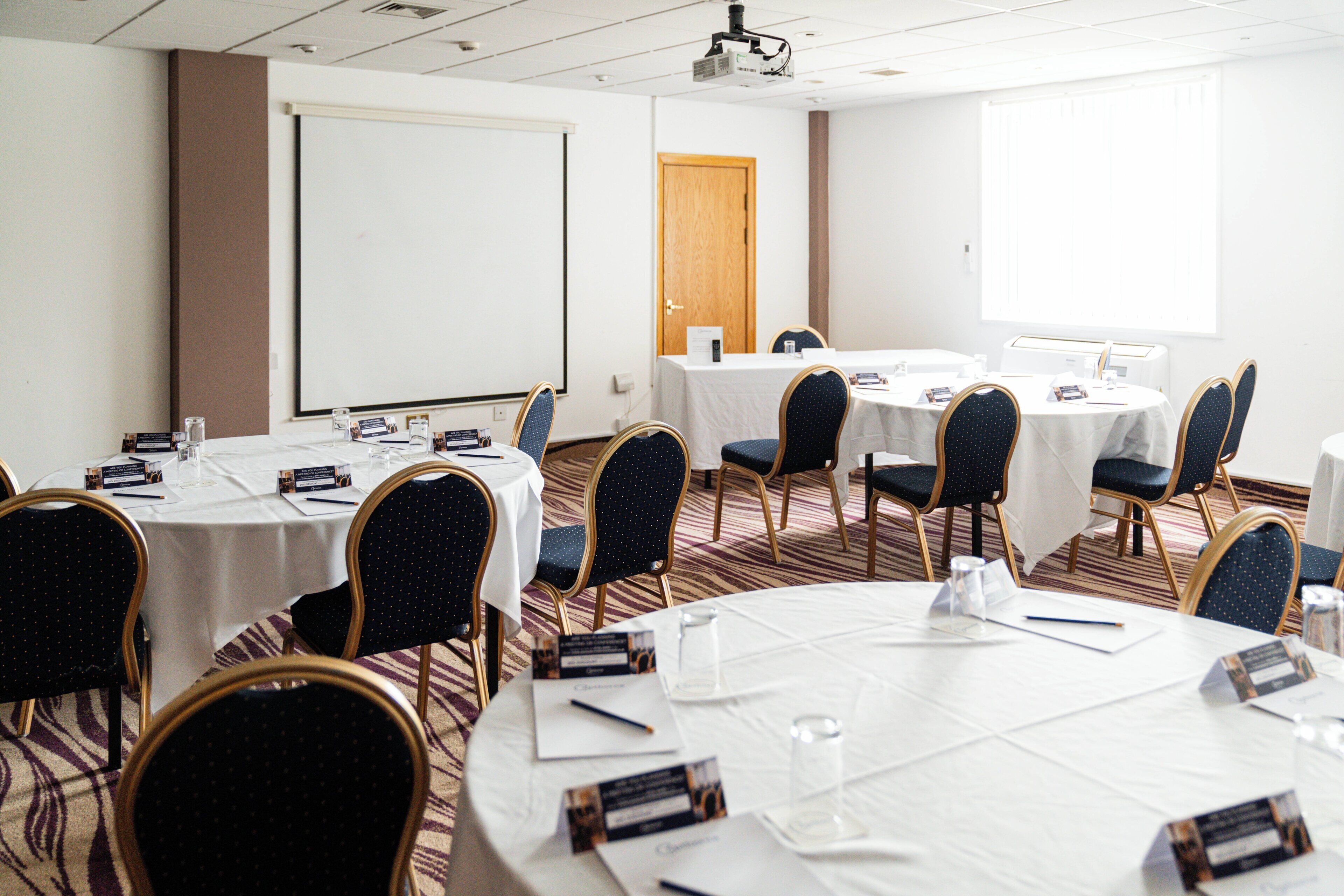 Une salle de conférence équipée de tables rondes, de porte-noms et d’un écran de projection.