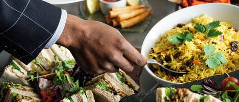 Un bufé con diversos platos, incluyendo sándwiches, una ensalada y un guiso de arroz.
