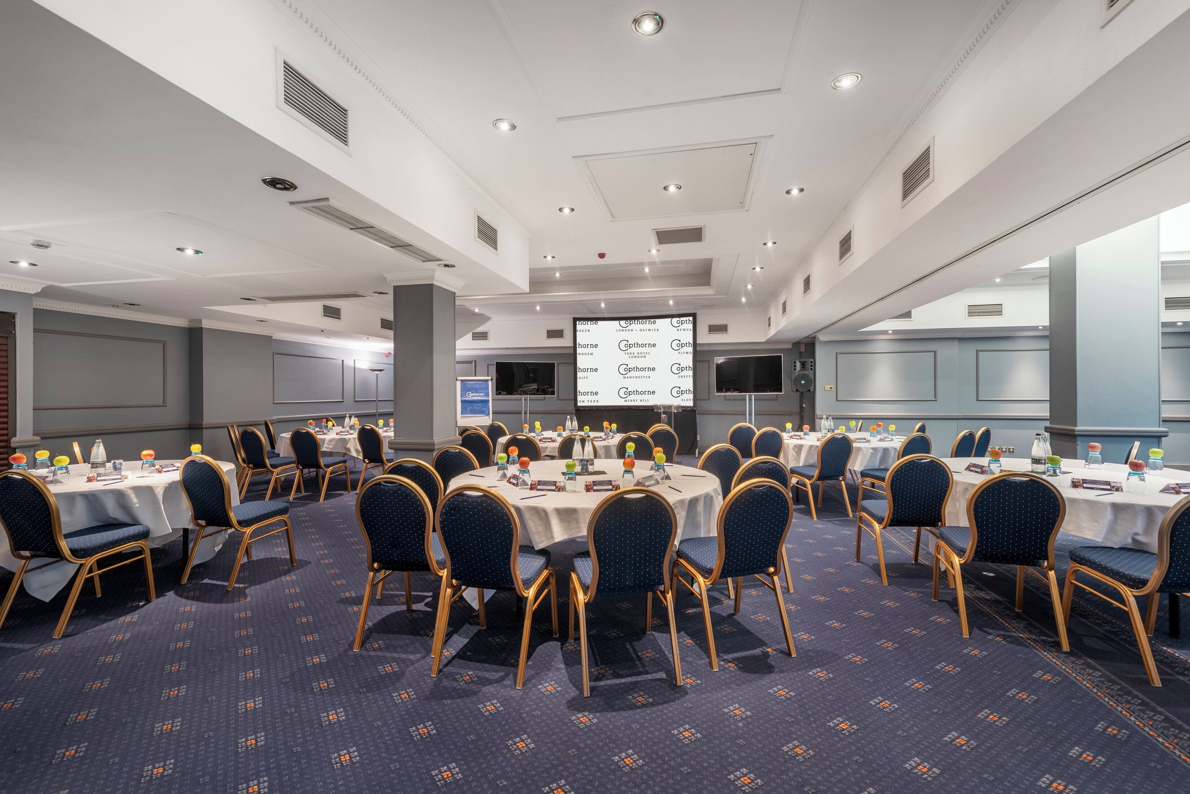 A conference room with round tables, chairs, and a projector screen displaying a presentation.