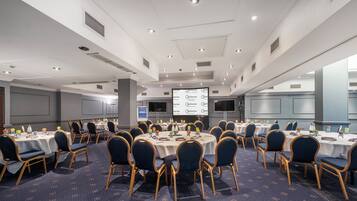 A conference room with round tables, chairs, and a projector screen displaying a presentation.