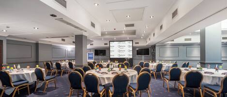 A conference room with round tables, chairs, and a projector screen displaying a presentation.