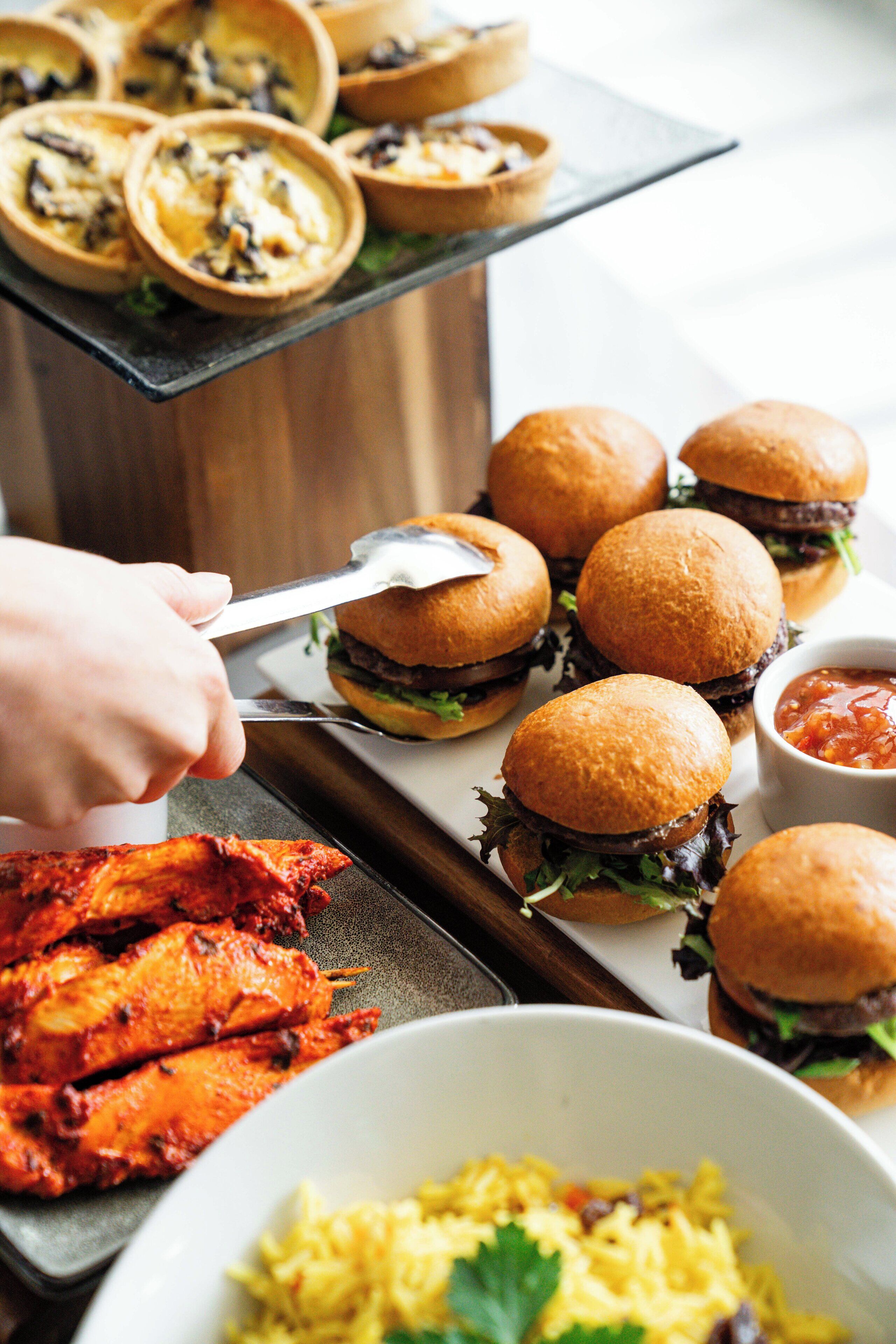 A buffet with various dishes including burgers, chicken wings, and rice.