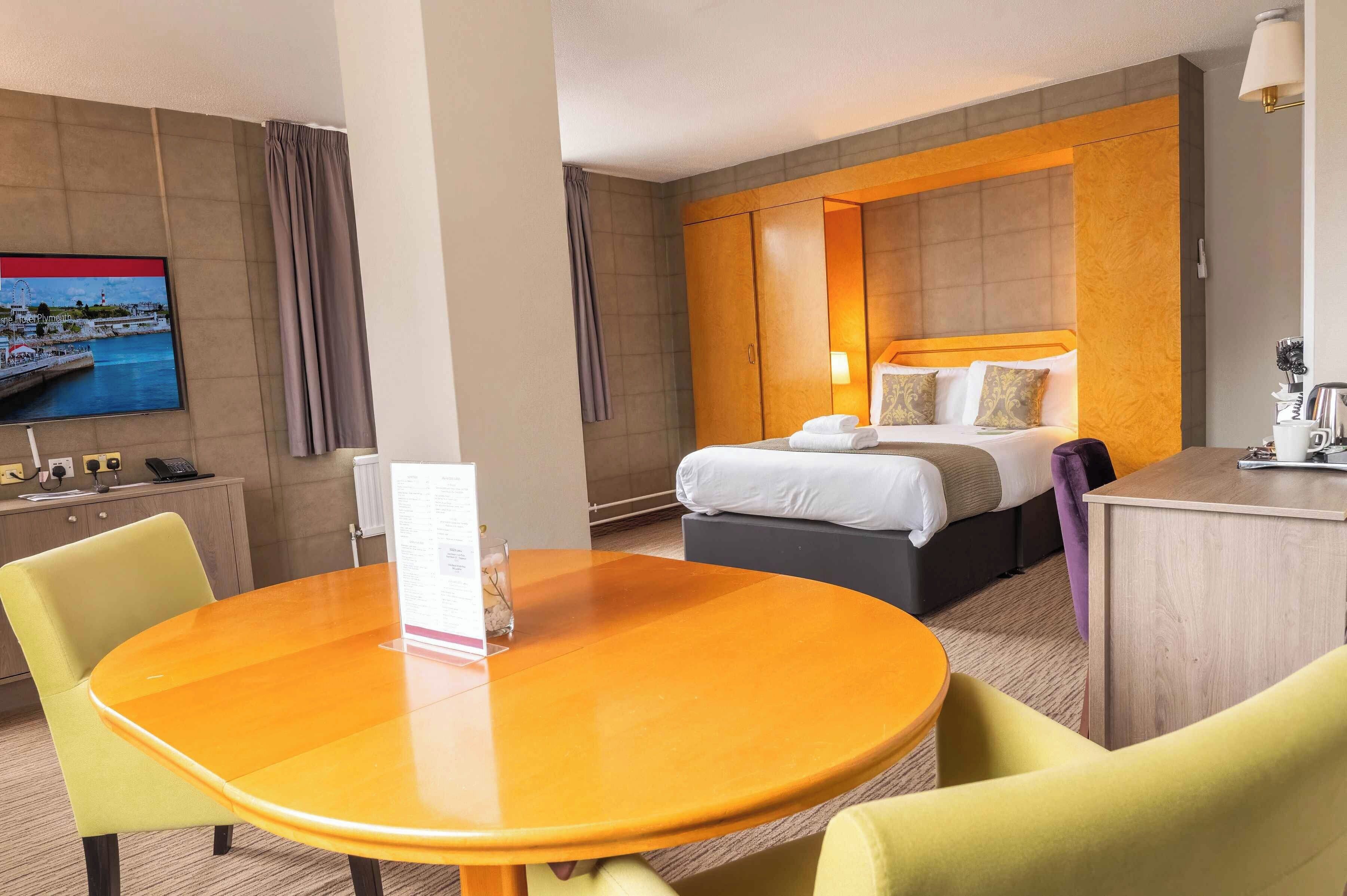 Una habitación de hotel con una cama, un escritorio, un televisor y una mesa de comedor con sillas.