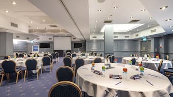 A conference room with multiple round tables, chairs, and presentation screens.