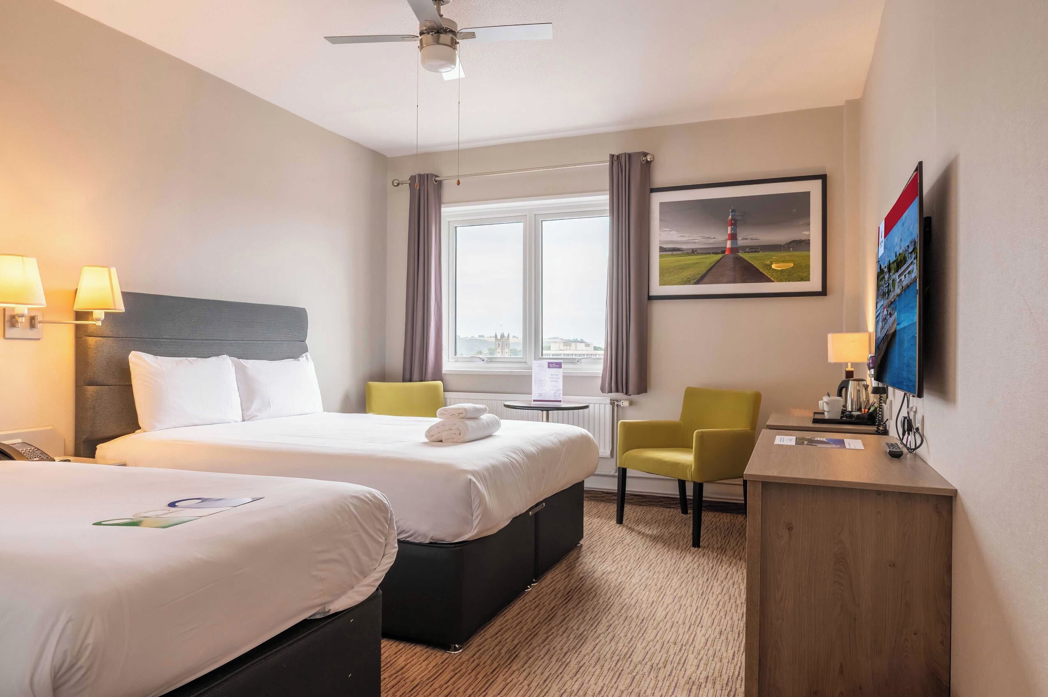 A hotel room with two beds, a desk, a chair, a TV, and a window with curtains.