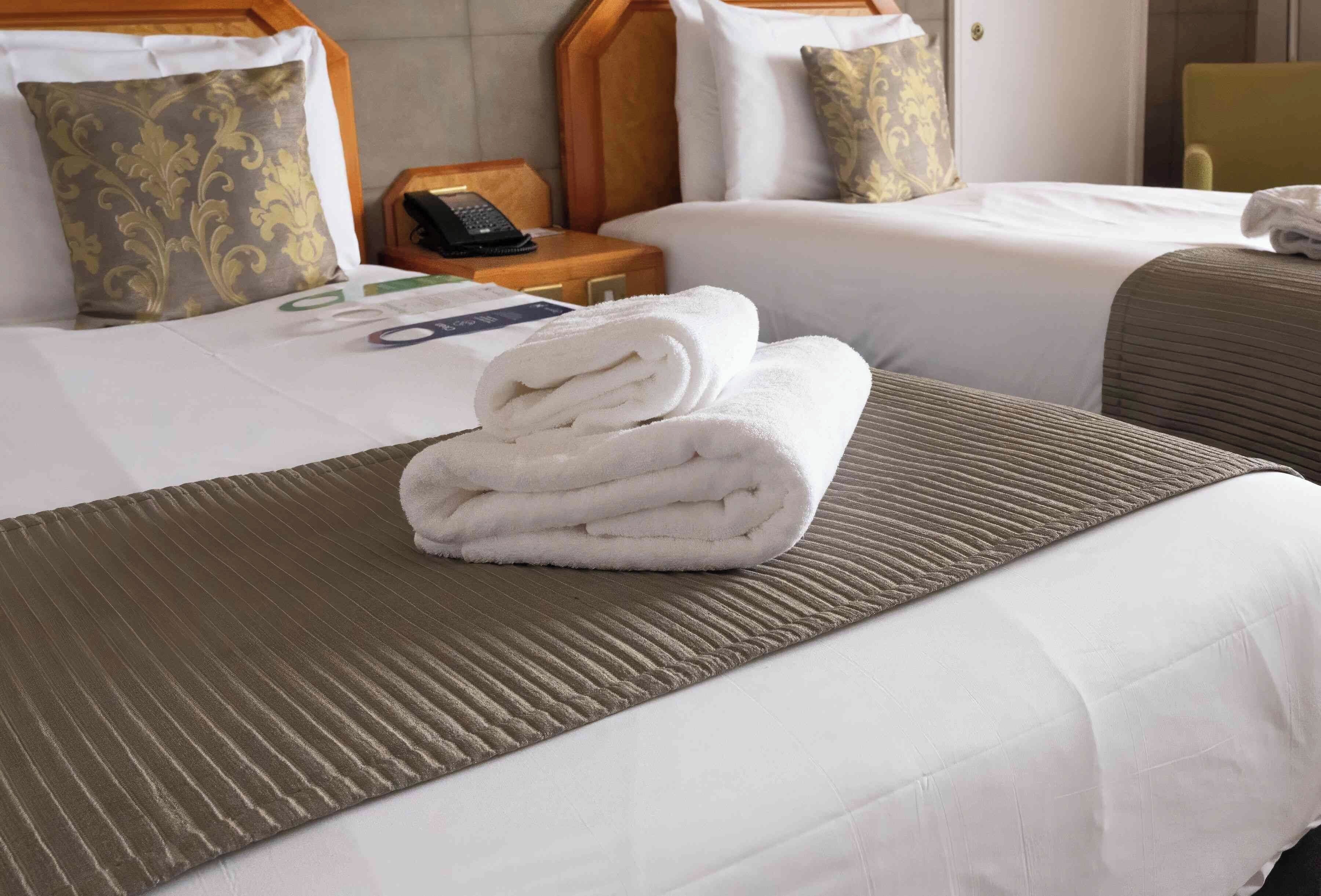 Une chambre d’hôtel avec deux lits, une table de chevet en bois avec un téléphone et une serviette pliée posée sur le lit.