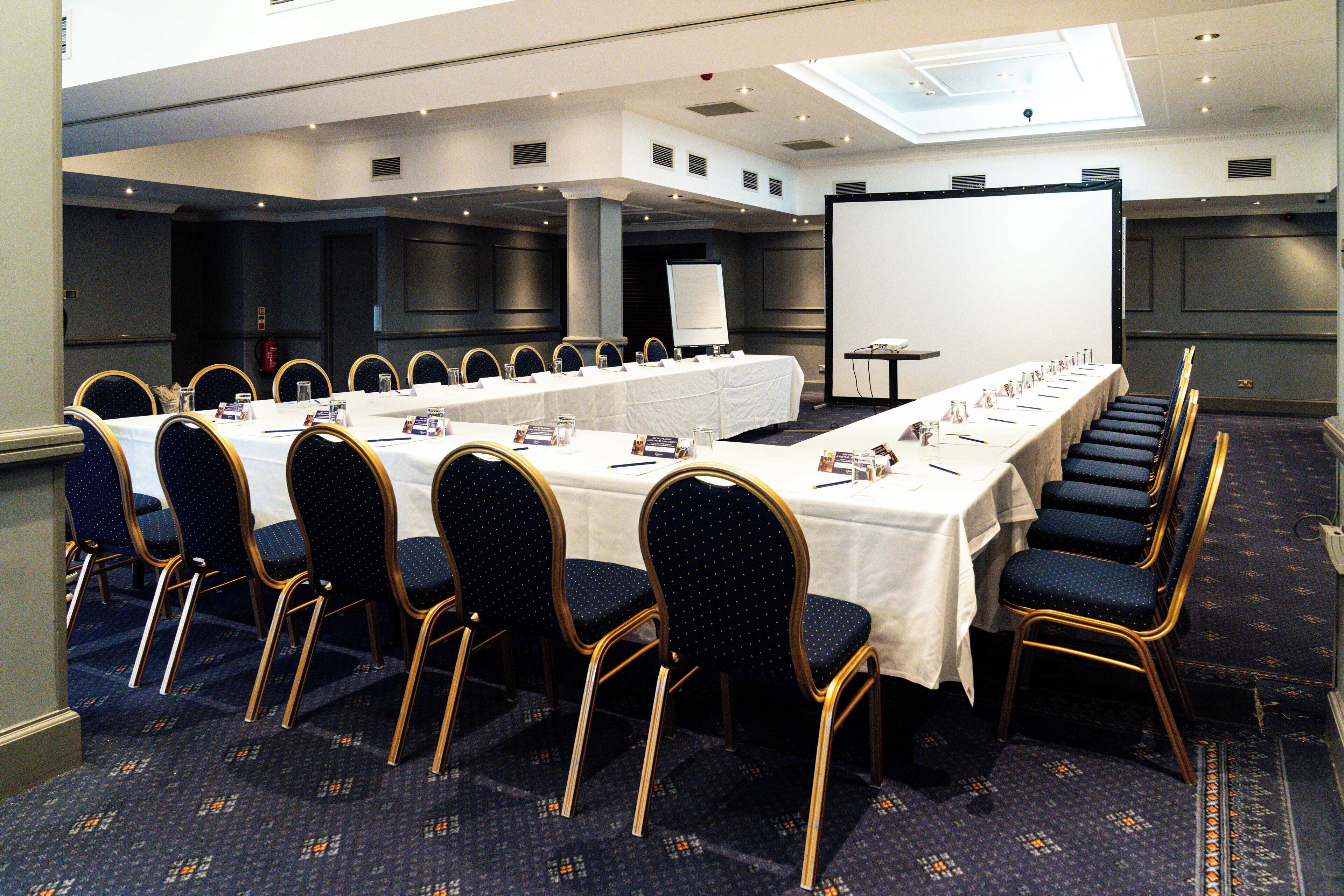 A conference room with a long table, rows of chairs, a projector screen, and a whiteboard.