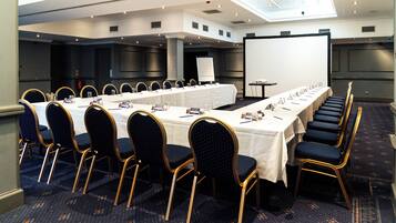 A conference room with a long table, rows of chairs, a projector screen, and a whiteboard.