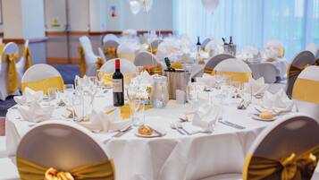 A banquet hall with round tables set for a formal event, featuring white tablecloths, gold sashes, and neatly arranged dining ware.