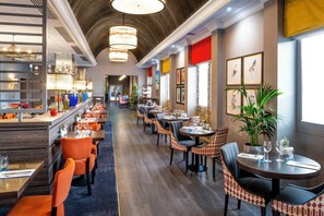 Un restaurant doté d’un long comptoir, de nombreuses tables et des chaises. On y trouve des éclairages décoratifs et un sapin de Noël.