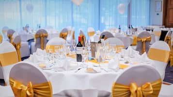 A banquet hall with round tables set for a formal event, featuring white tablecloths and gold sashes on chairs.