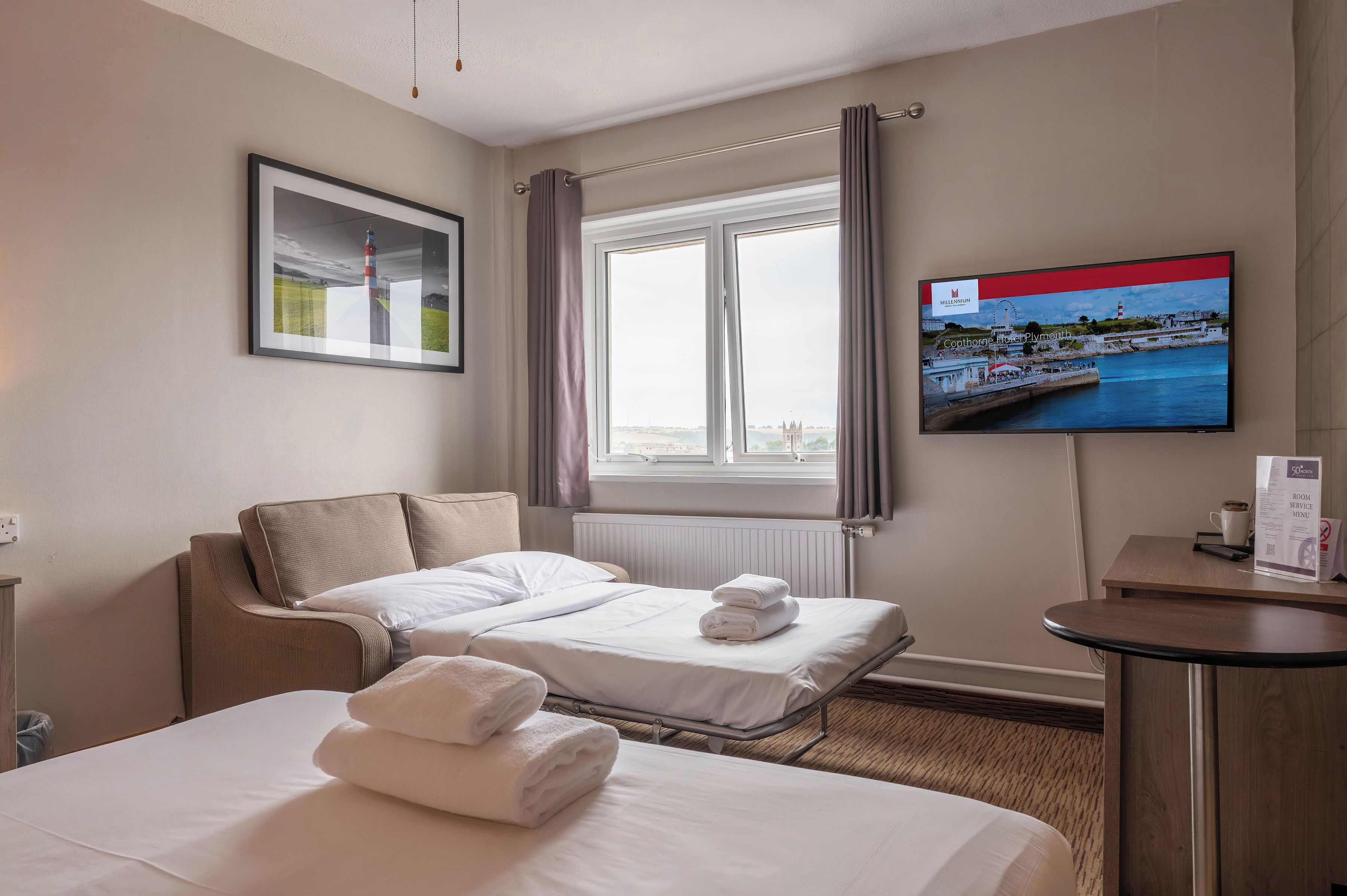A hotel room with two beds, a television, a framed picture, and a window with curtains.