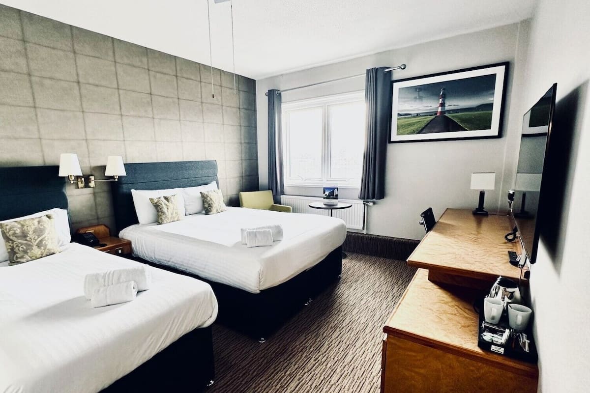 Ein Hotelzimmer mit zwei Betten, einem Schreibtisch, einem Stuhl, einem Fernseher und einem Fenster mit Vorhängen.