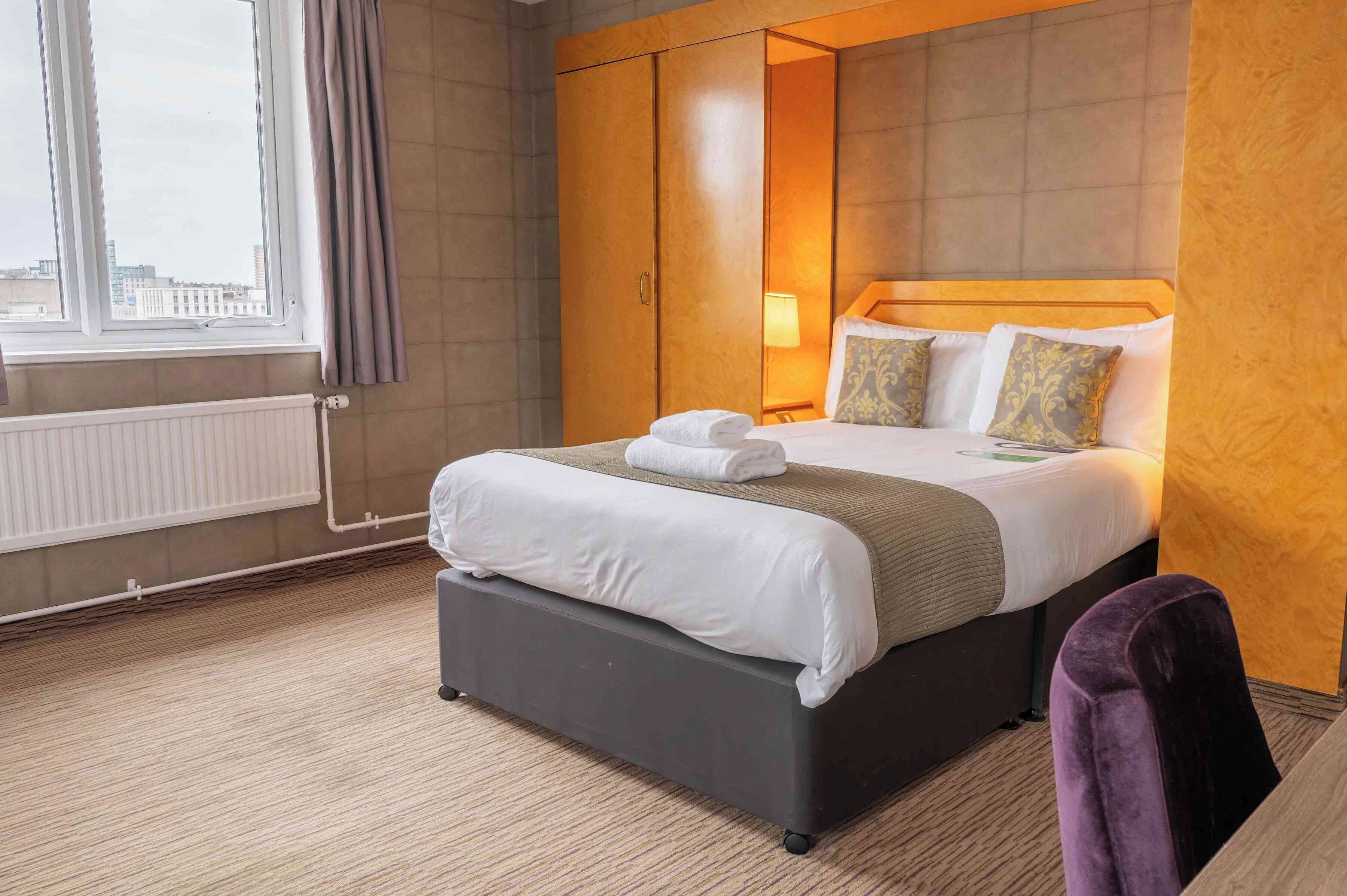 Ein Hotelzimmer mit einem großen Bett, einem Kleiderschrank, einem Fenster mit Vorhängen und einem Heizkörper.
