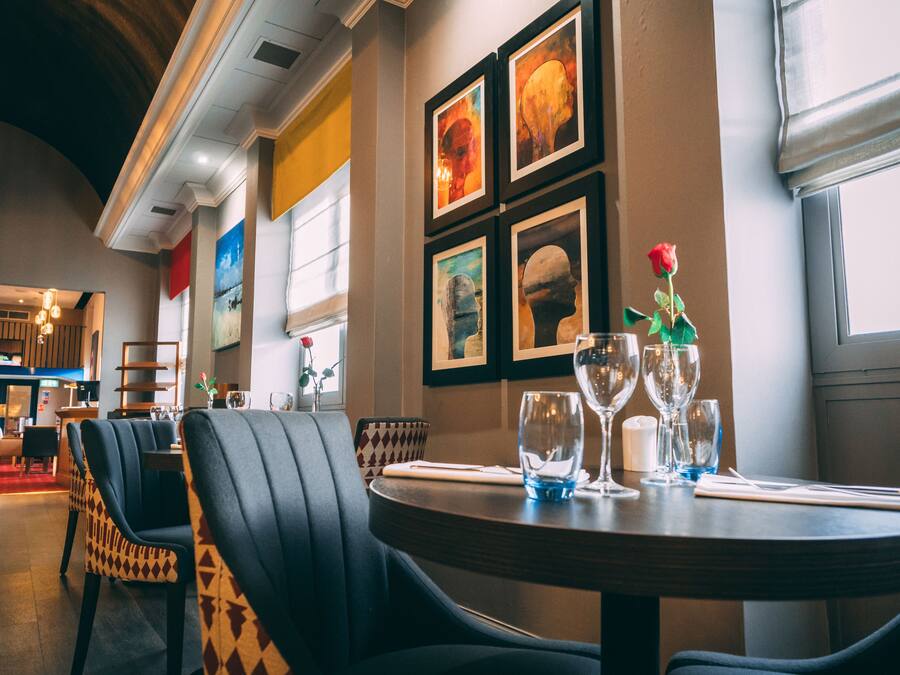 A restaurant interior with round tables, black upholstered chairs, and framed artwork on the walls.