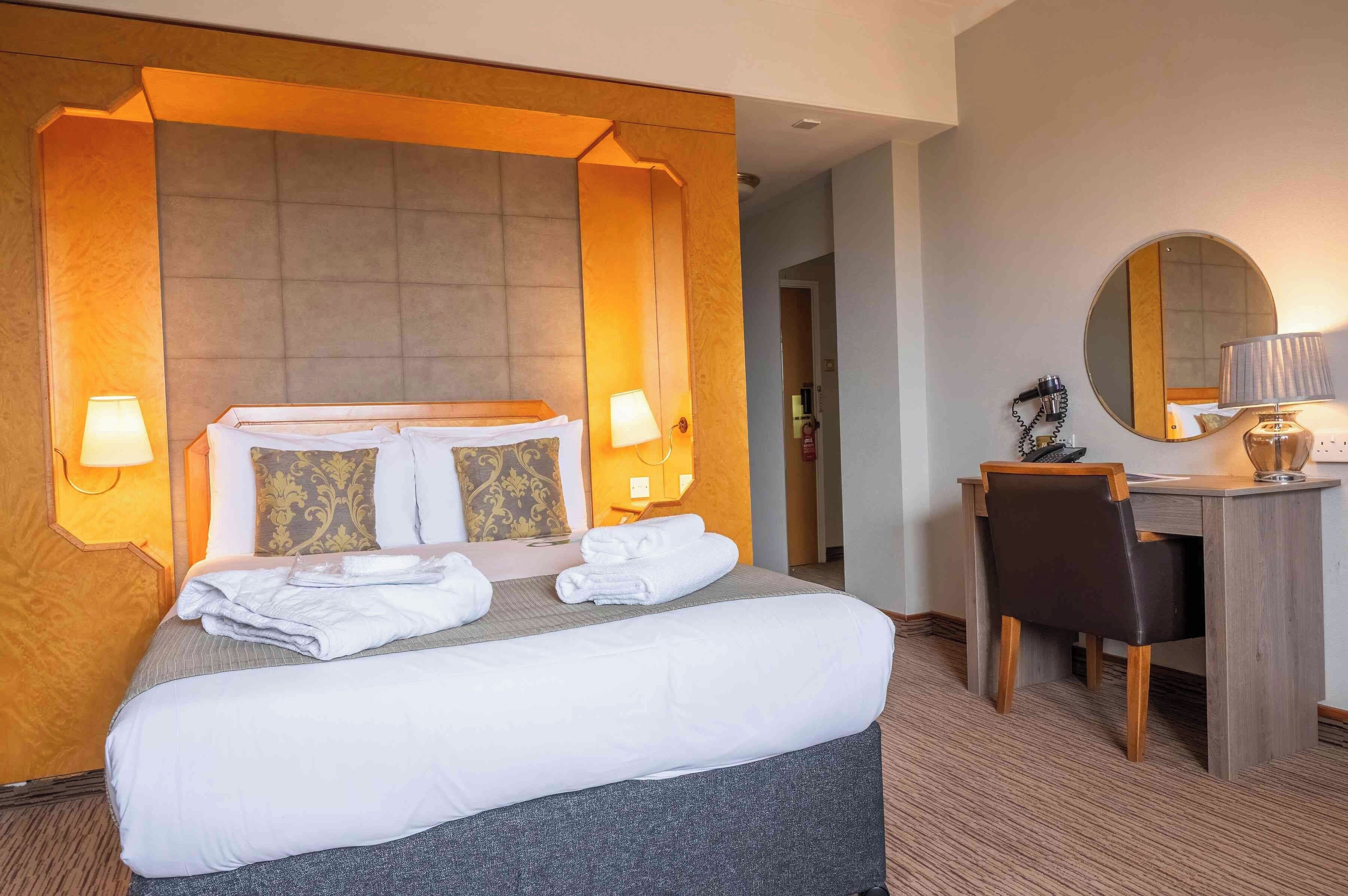 Une chambre d’hôtel avec un grand lit, deux lampes de chevet, un bureau avec une chaise, un miroir rond et un téléphone fixé au mur.