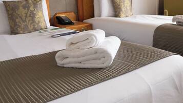 Una habitación de hotel con dos camas, una mesita de noche de madera con un teléfono y una toalla doblada sobre la cama.
