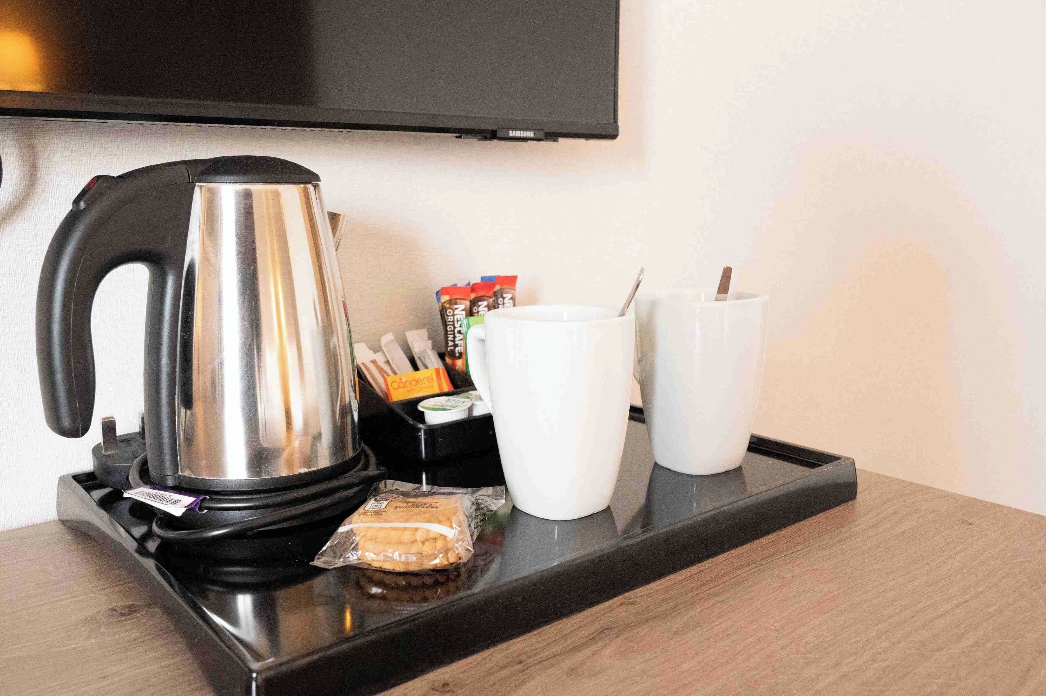 Een dienblad met een waterkoker, koffiekapsules en twee witte mokken op een houten ondergrond.