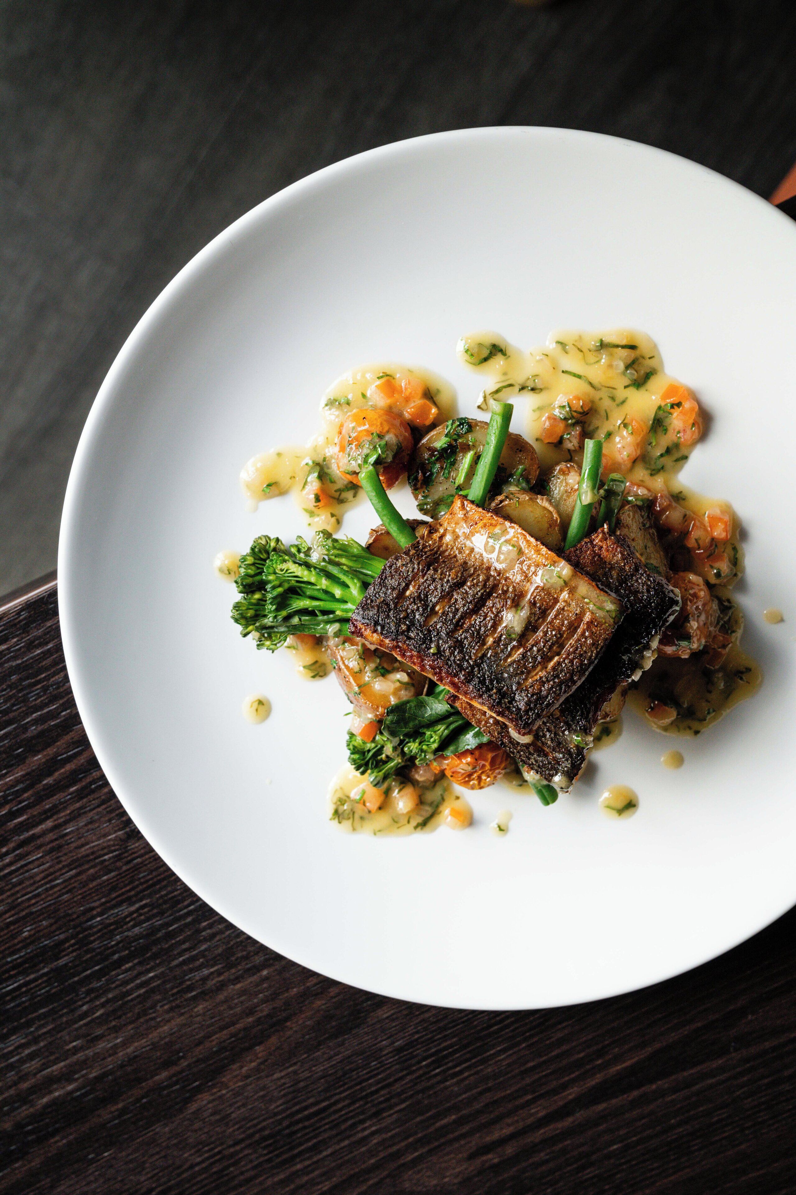 A white plate with a piece of grilled fish, broccoli, and potatoes.