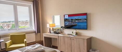 Habitación de hotel con cama, escritorio, silla, televisor y ventana con vistas a edificios.