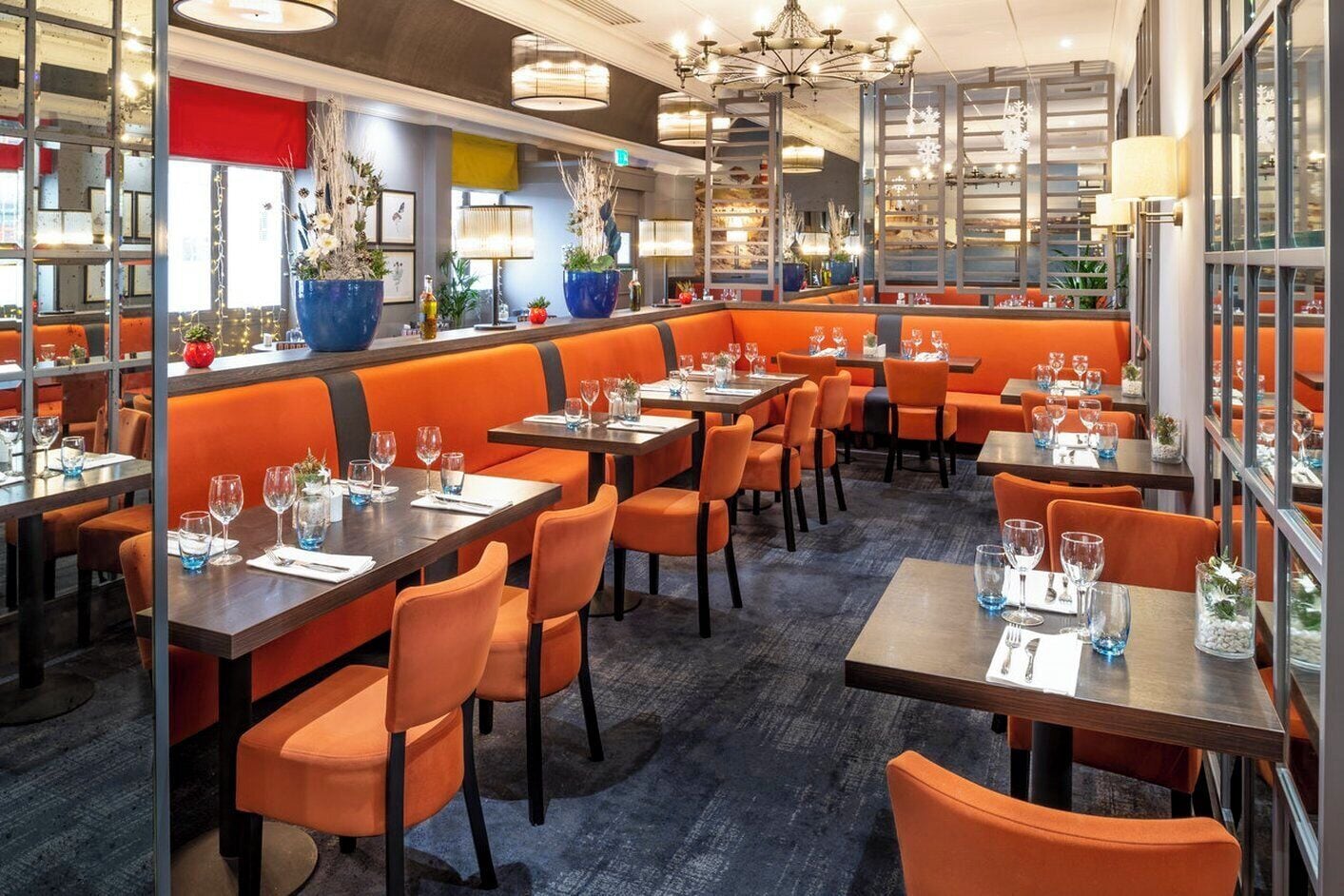 A restaurant with orange booths and tables, large windows, and decorative plants.