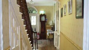 A hallway with a patterned rug, a staircase, and a clock on the wall. - Clanabogan Country House B&B (Omagh)