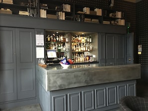 A bar area with a counter, shelves of bottles, and a computer monitor.