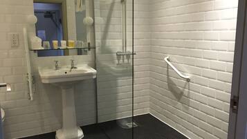 Un baño moderno con azulejos blancos tipo metro, cabina de ducha de vidrio, lavamanos pedestal y barandilla.