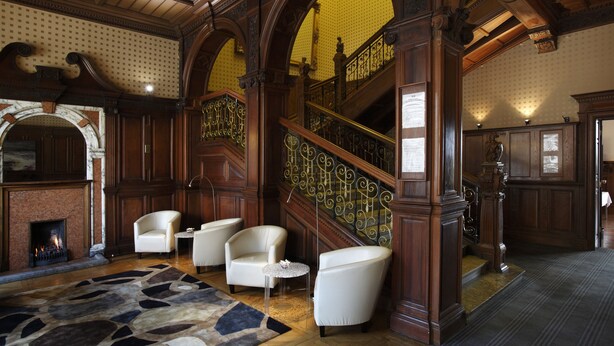 A grand lobby with a fireplace, a staircase with ornate railings, and a seating area with white armchairs. - B+B Edinburgh (Edinburgh)
