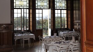A dining area with tables and chairs, large windows with stained glass, and a view of trees and buildings outside. - B+B Edinburgh (Edinburgh)