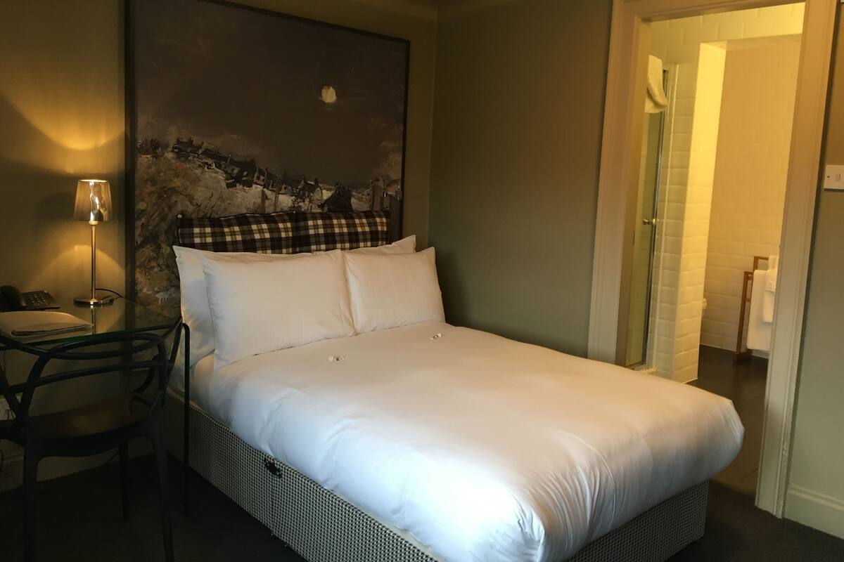 Una cama bien hecha con sábanas blancas, una almohada a cuadros y un cuadro colgado en la pared.