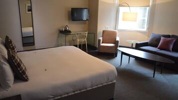 Une chambre d’hôtel avec un grand lit, un canapé, un fauteuil, une petite table, une télévision et une fenêtre avec une lampe.