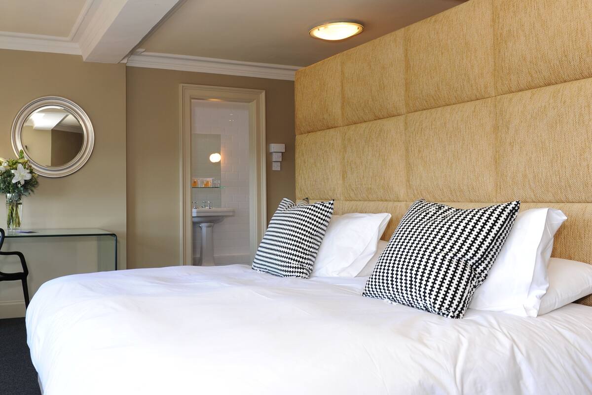 Habitación de hotel con una cama grande, un escritorio con silla, un espejo y la puerta del baño.